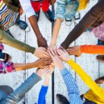 Kurse & Workshops Blick auf Menschen, die im Kreis stehen und ihre Hände in der Mitte feierlich aufeinanderlegen